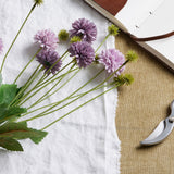 Hill Interiors Purple Chrysanthemum Bouquet with layered pompom heads and green leaves, styled on white linen beside an open leather journal and secateurs.