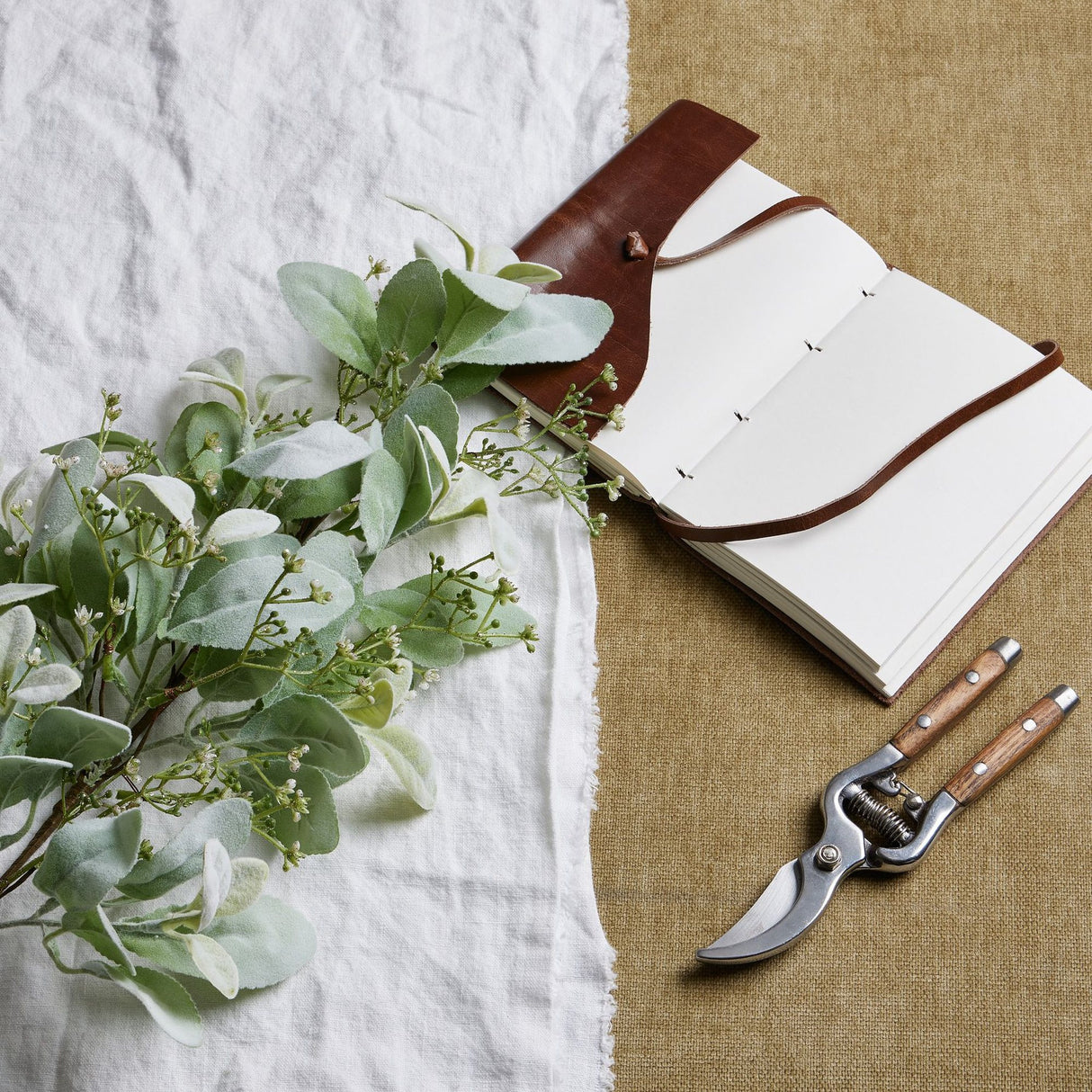Hill Interiors large winter sprig with velvety lambs ear leaves and wax flower sprays, styled beside an open leather journal and wooden-handled secateurs.