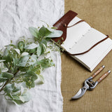 Hill Interiors large winter sprig with velvety lambs ear leaves and wax flower sprays, styled beside an open leather journal and wooden-handled secateurs.
