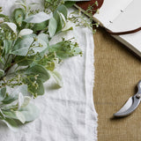 Hill Interiors large winter sprig with velvety lambs ear leaves and fine wax flower sprays on a white linen cloth beside an open leather journal and secateurs.