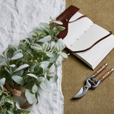 Winter spray arrangement with lambs ear leaves and wax flower sprigs, tied with hessian ribbon beside a leather journal and wooden-handled secateurs.