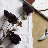 Hill Interiors Tall Black Poppy Stem faux flowers with crinkled petals and green leaves on white linen beside an open leather journal and pruning shears.