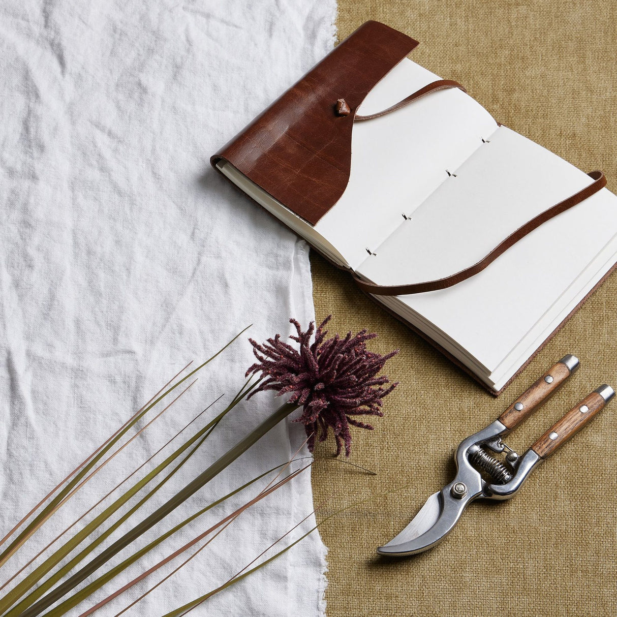 Hill Interiors Burgundy Aster Spider Chrysanthemum Stem with slender curling petals, shown beside a leather journal and wooden-handled secateurs on linen.