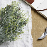 Hill Interiors Frosted Pine Spray Stem with pinecones laid on a white linen cloth beside an open leather-bound journal and metal secateurs.