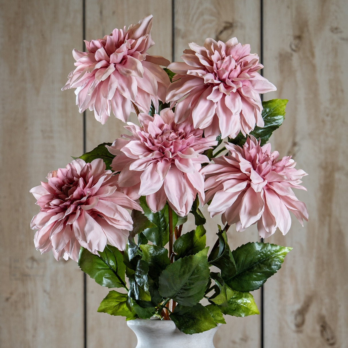 Hill Interiors Pink Dahlia faux flower stem with layered blush petals and green leaves, displayed in a white vase against a light wood panel background.