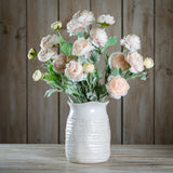 Hill Interiors Pink Ranunculus faux stems with layered blush petals and green foliage, arranged in a white textured ceramic vase against a wooden backdrop.