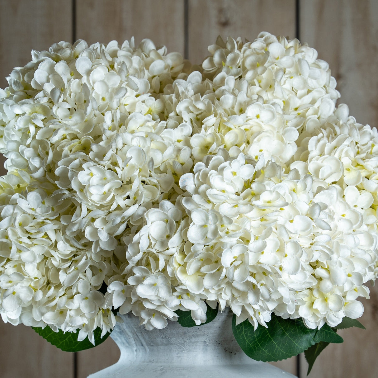 Hill Interiors White Allium faux stems with dense clusters of small white florets, arranged in a pale stone vase against a wooden plank background.
