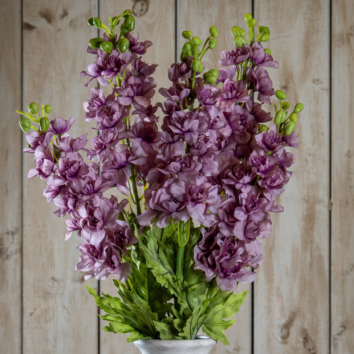 Hill Interiors Purple Elatum Delphinium faux stems with ruffled two-tone purple florets and green buds, displayed against a light wooden plank background.