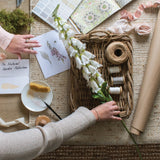 Hill Interiors White Foxglove faux stem with tall spires of speckled bell blooms, styled on a woven mat with wicker tray, twine and ribbons.
