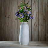 Hill Interiors Purple Scabious Stem arranged in a tall stone-effect vase on a wooden surface against a rustic timber plank background.