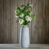 Hill Interiors White Scabious Stem arranged in a tall pale stone vase against a rustic wooden plank backdrop, showing ruffled white blooms and green foliage.
