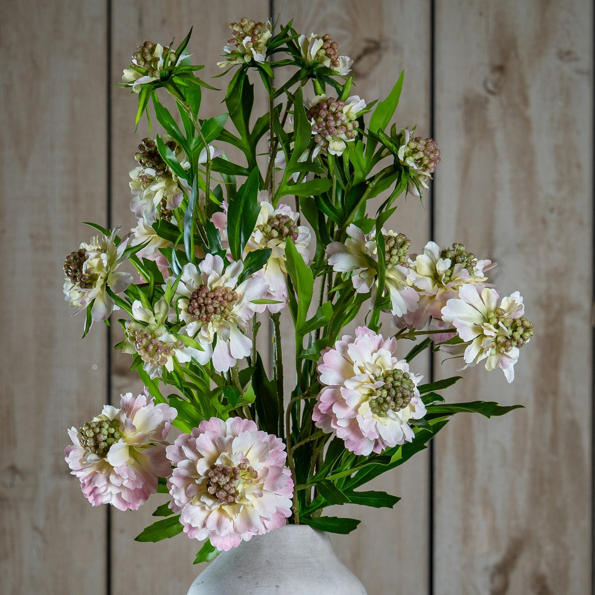 Hill Interiors Pale Pink Scabious Stem faux arrangement with layered blush petals and textured centres, displayed in a stone vase against wooden panelling.