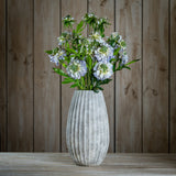 Hill Interiors Pale Blue Scabious Stems arranged in a ribbed grey stone vase on a wooden surface against a wood plank background.