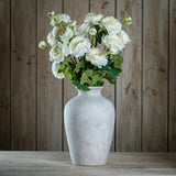 Hill Interiors Apricot Ranunculus faux stems arranged with green foliage in a whitewashed ceramic urn vase against a wooden plank backdrop.