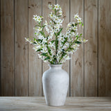 Hill Interiors Turks Cap Green Lily Spray arranged in a tall stone vase against a rustic wood plank background.