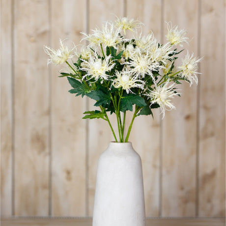Hill Interiors Cream Sea Holly Spray with spiky cream bracts and green foliage arranged in a tall white ceramic vase against a wooden panel backdrop.