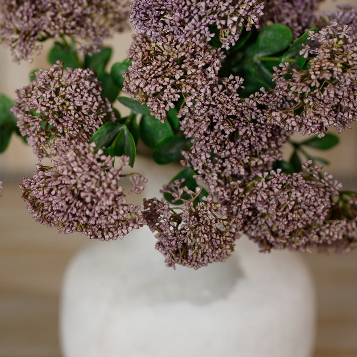 Hill Interiors Purple Sedum Spray with clustered dusky mauve florets and green leaves arranged in a white ceramic vase.