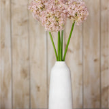 Hill Interiors Lilac Giant Allium Stems arranged in a tall white ceramic vase against a light wood panel background.