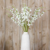 Hill Interiors White Cymbidium Spray arranged in a tall white ceramic vase, showing arching stems of small white orchid blooms against a wood plank backdrop.