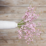 Hill Interiors Lilac Cymbidium Spray arranged in a white vase against a pale wood-panelled wall, with arching stems of soft purple orchid blooms.