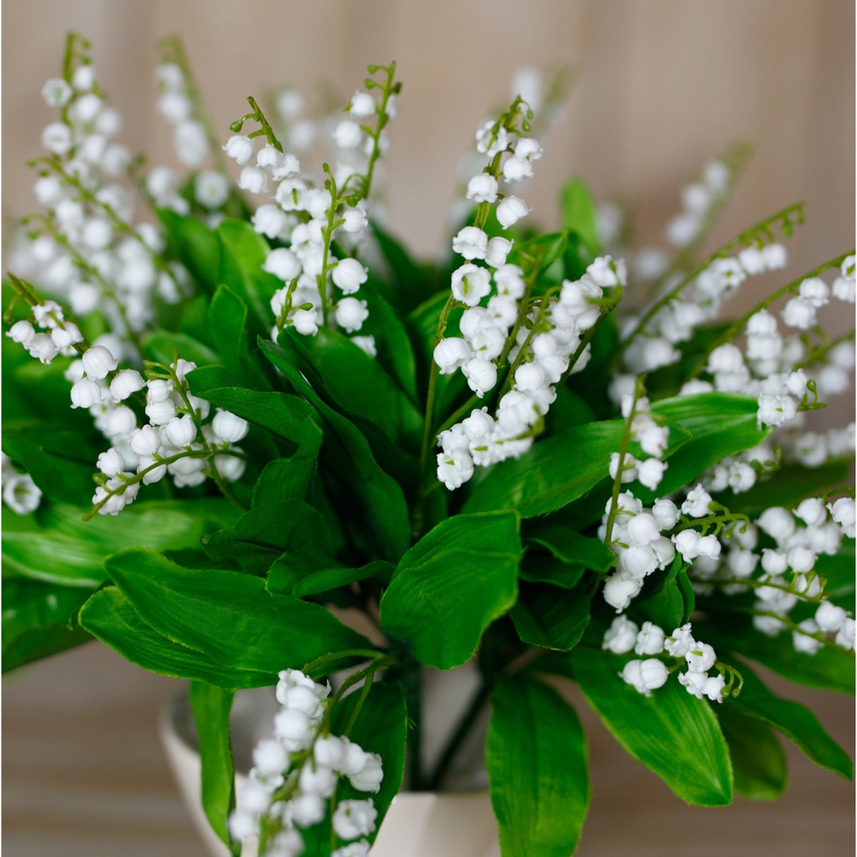 Close-up of Hill Interiors Lily of the Valley Bunch faux plant, showing tiny white bell-shaped blooms on slim stems arching above bright green leaves.