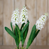 Hill Interiors White Hyacinth Stem faux flowers with clustered star-shaped florets and green leaves, displayed against a light wood panel background.