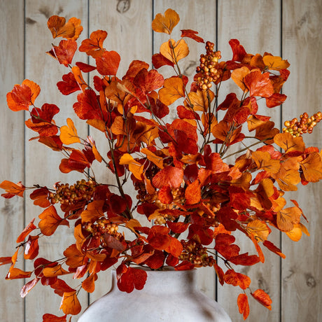 Hill Interiors Large Autumn Spray with Berries in a stone vase, showing layered orange and red foliage with berry clusters against a wooden plank backdrop.