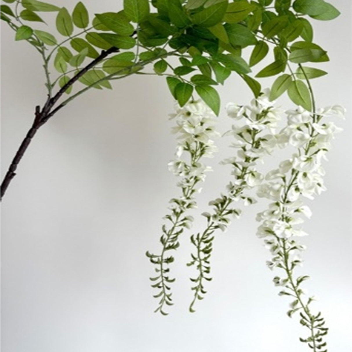 Hill Interiors Large White Wisteria Spray with trailing white bloom racemes and green leaves on a dark stem, shown against a plain light background.