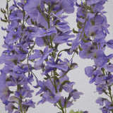 Close-up of Hill Interiors Large Purple Wisteria Spray showing cascading clusters of ruffled lilac blooms and small green leaves along trailing stems.