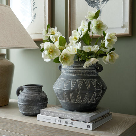 Hill Interiors White Hellebore Stem arranged in a black patterned ceramic vase on stacked books, styled beside a smaller jug and lamp on a console.