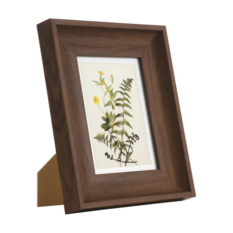 Renabie Photo Frame 21 x 26cm in walnut-effect wood with wide bevelled moulding, displaying a botanical print of fern and yellow flowers, shown at an angle on a white background.