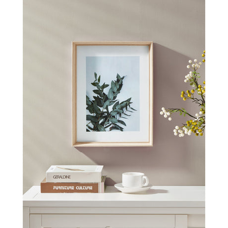 Renabie Photo Frame, 32.5 x 42.5cm, in an oak effect wood finish with a white mount, displaying a green foliage print, hung on a wall above a white console table.