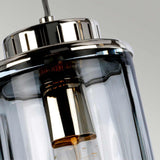 A close-up of the Reno 1 Light Pendant featuring a polished nickel top and smoke glass casing, showcasing the bulb inside. The pendant light is suspended by a cord against a plain background.