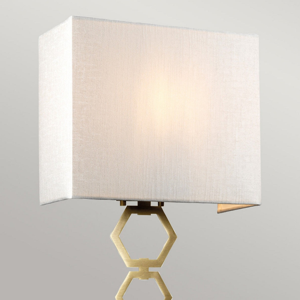 The Ria Medium 1 Light Wall Light, crafted in aged brass, showcases a modern aesthetic with its square ivory faux silk shade and is elegantly topped with an octagonal finial. It stands out beautifully against a plain gray background.