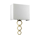 Introducing the Ria Medium 1 Light Wall Light in aged brass, which showcases a stylish ivory faux silk shade and a contemporary metal base composed of three connected hexagonal shapes, all elegantly finished with an octagonal finial.