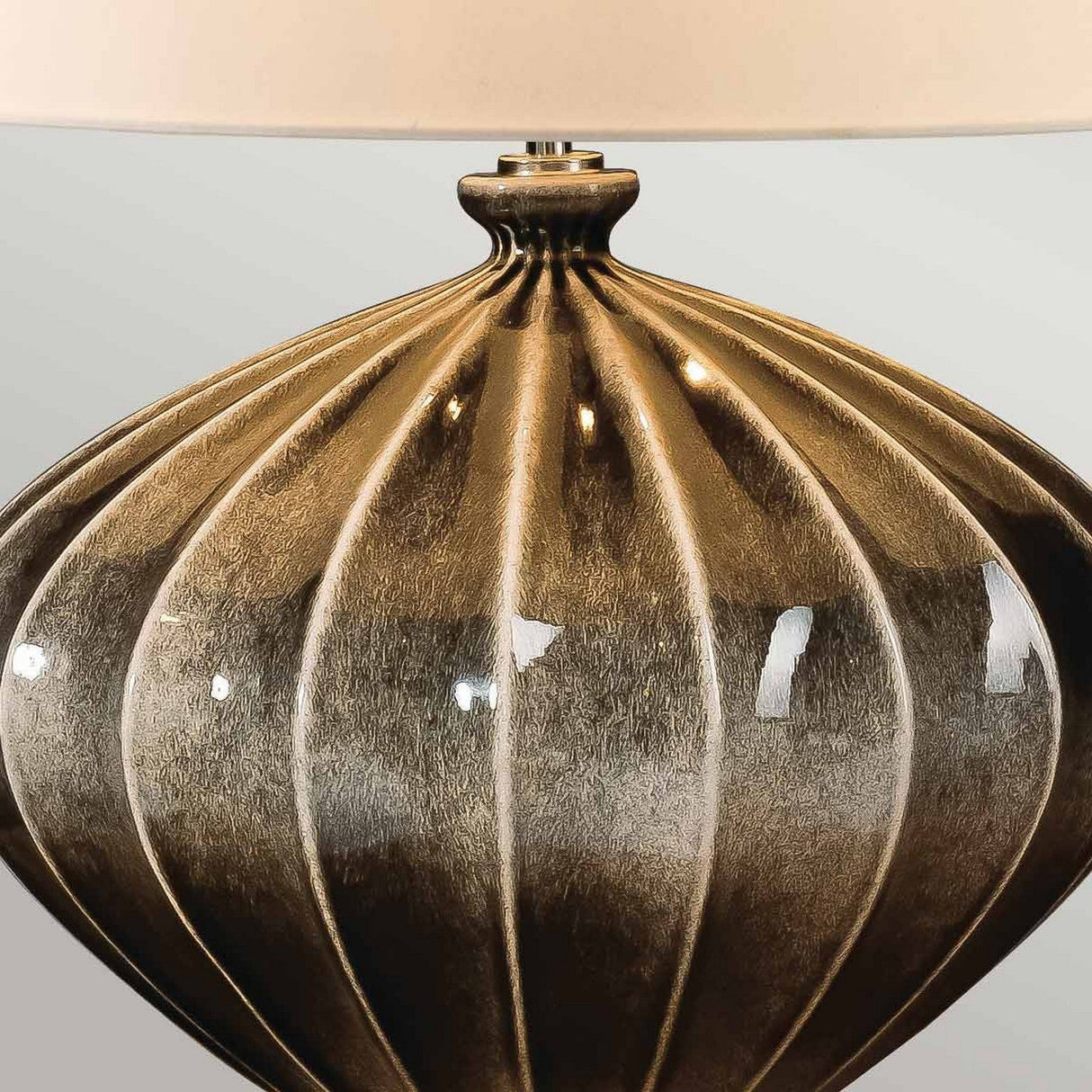 A detailed view of the Rib Pumpkin 1 Light Table Lamp showcases its textured, ribbed design on a metallic base in antique bronze color. A glimpse of the faux silk shade is visible at the top edge.