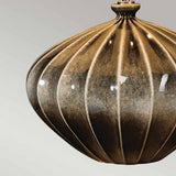 A close-up of the Rib Pumpkin 1 Light Table Lamp in a metallic shade with a warm golden-brown finish, featuring a dome-shaped design with a ribbed texture that beautifully reflects light. The background is a muted gray gradient, enhancing its elegance.