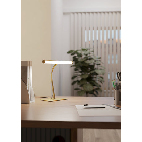 Riccione LED Touch Table Lamp in brushed brass, with tubular diffuser, ribbed gooseneck stem and flat base, shown illuminated on a desk in a home office setting.