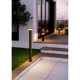 Rigosa Outdoor LED Floor Lamp in black, a slim bollard-style steel post with a flat disc cap, lighting a patio pathway beside wooden decking steps at dusk.