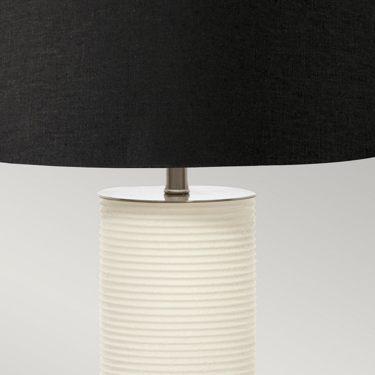 Introducing the Ripple 1 Light Table Lamp, showcasing a modern off-white ceramic base with ribbed detailing and paired with a sophisticated black fabric shade. This contemporary lighting piece is set against a neutral gray backdrop, making it an ideal addition to enhance any interior decor.