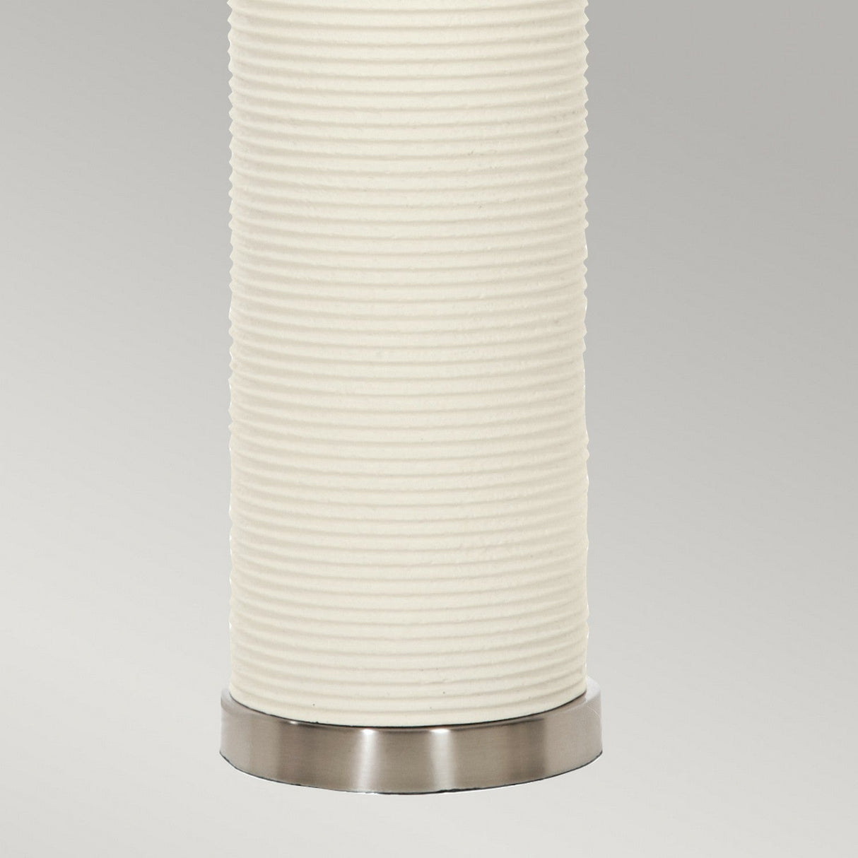 A close-up of the Ripple 1 Light Table Lamp, featuring a tall, cylindrical modern design with a textured and ribbed white surface atop a metallic base, set against a plain light gray background.