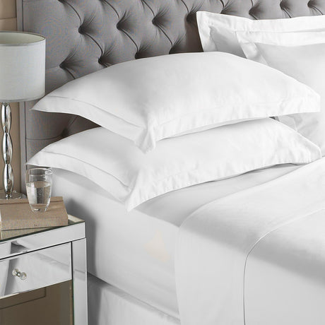 White cotton percale fitted sheet dressed on a bed with matching pillowcases, styled with a grey buttoned headboard in a bedroom setting.