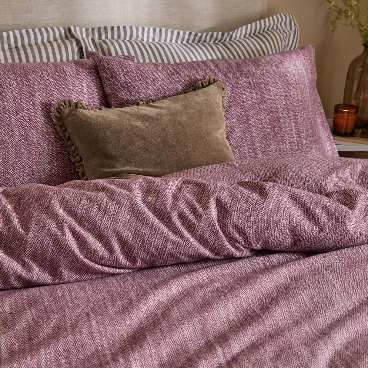 Harris Cotton Herringbone Duvet Cover Set in beetroot on a bed, with striped pillowcases and a brown velvet ruffled cushion in a bedroom setting.
