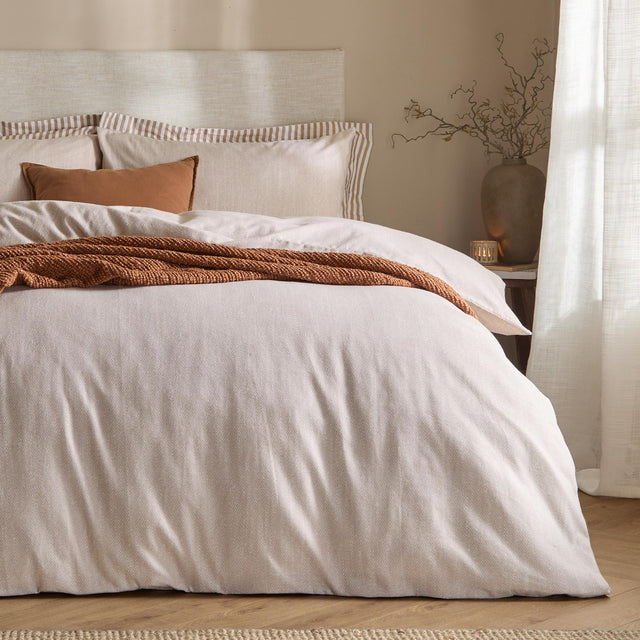Harris Cotton Herringbone Duvet Cover Set in natural on a bed with striped and plain pillows, styled with a rust knitted throw in a neutral bedroom setting.