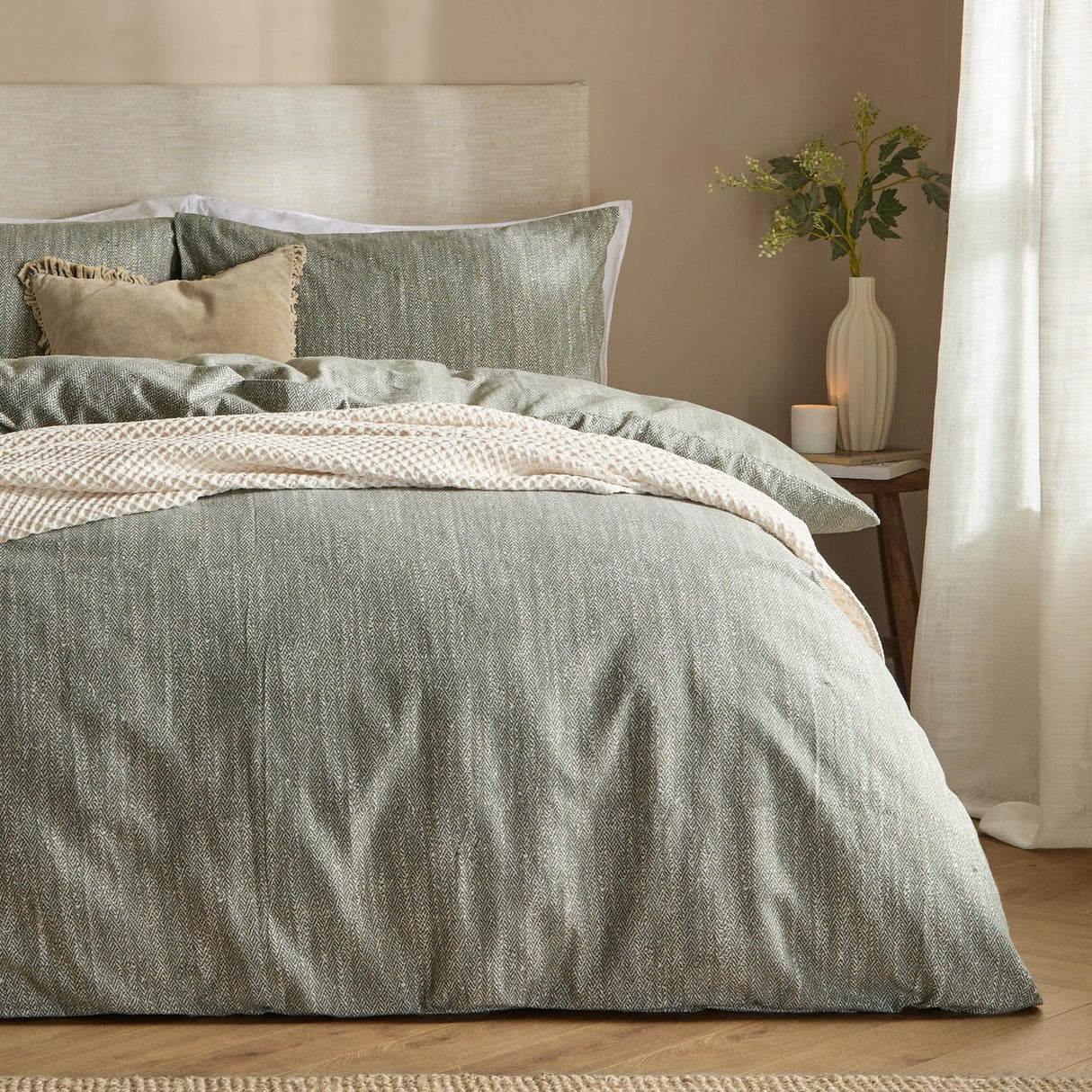 Harris Cotton Herringbone Duvet Cover Set in olive dressed on a bed with matching pillowcases and a cream throw, styled in a neutral-toned bedroom.
