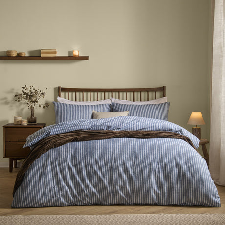 Holme Stripe Cotton Brushed Duvet Cover Set in denim blue with white pinstripes, styled on a bed with matching pillowcases, a cushion, and a draped throw in a bedroom setting.