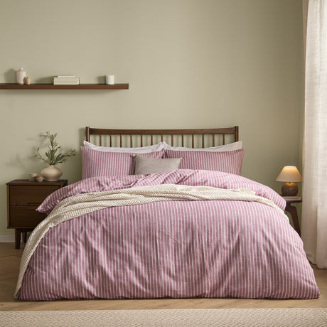 Holme Stripe Cotton Brushed Duvet Cover Set in Rosewood, a fine white striped design on a dusky pink ground, dressed on a bed with matching pillowcases in a bedroom setting.