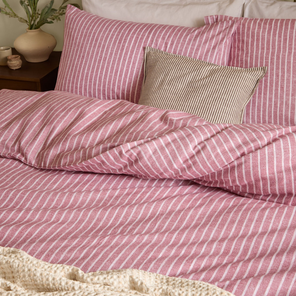 Holme Stripe Cotton Brushed Duvet Cover Set in Rosewood, a fine white striped pattern on a dusky pink ground, shown on a bed with matching pillowcases and a striped cushion.