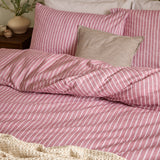Holme Stripe Cotton Brushed Duvet Cover Set in Rosewood, a fine white striped pattern on a dusky pink ground, shown on a bed with matching pillowcases and a striped cushion.