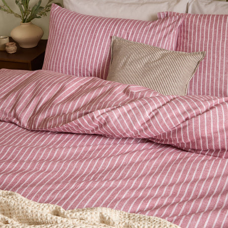 Holme Stripe Cotton Brushed Duvet Cover Set in Rosewood, a fine white striped pattern on a dusky pink ground, shown on a bed with matching pillowcases and a striped cushion.